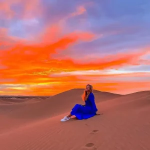 Woman in a blue dress sitting on a Sahara sand dune at sunset